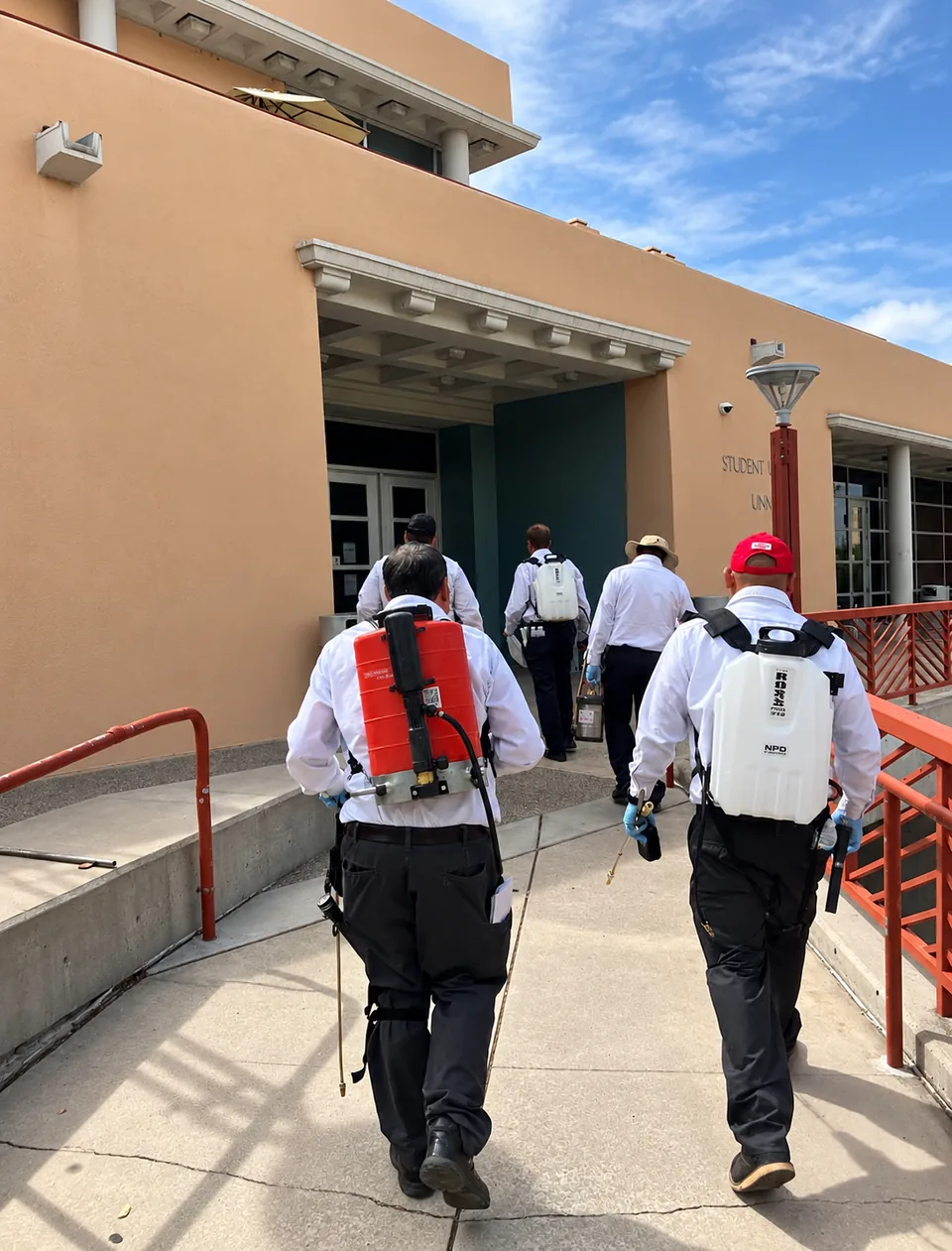 Team carrying pest control equipment towards a building entrance